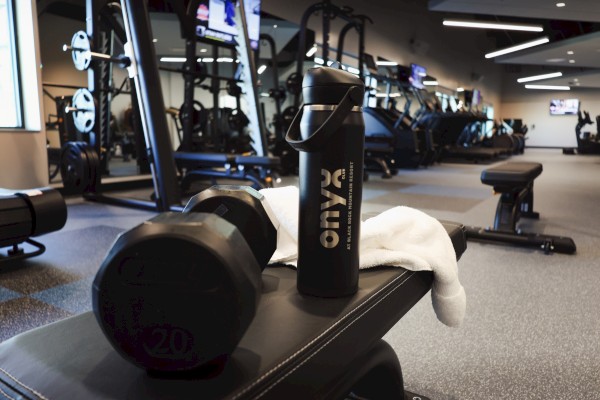 A gym workout area with dumbbells, a water bottle, and workout equipment in the background.