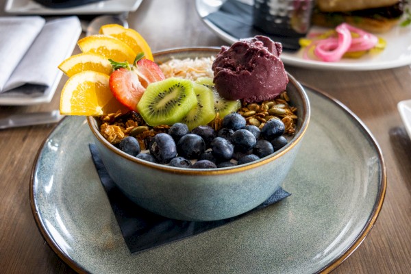 A bowl of yogurt topped with blueberries, sliced kiwi, strawberries, orange slices, granola, and a scoop of berry sorbet.