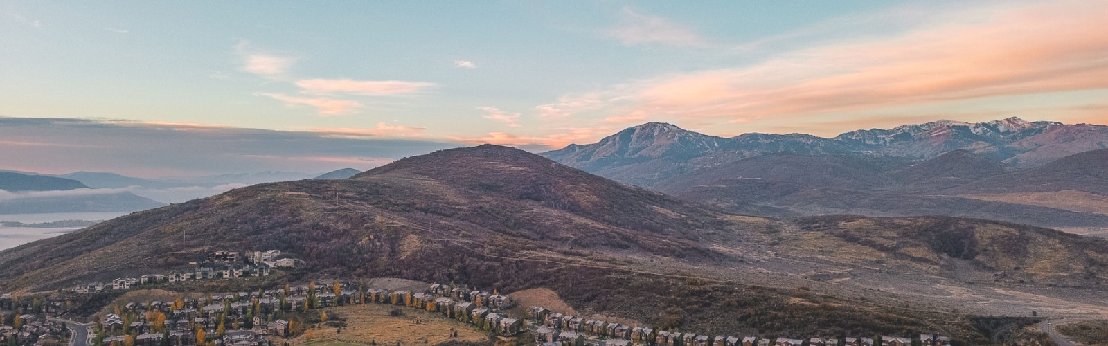 A panoramic view of a hilly residential area with mountains in the background during sunset.