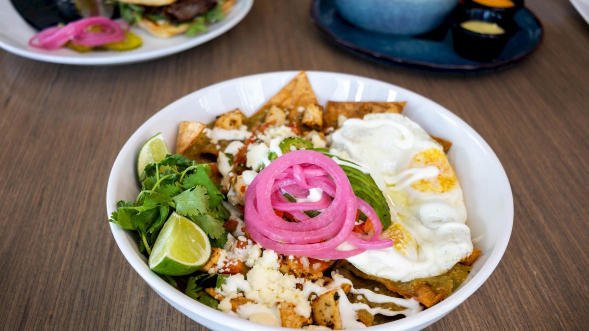 A colorful Mexican dish with jalapeños, cilantro, lime, pickled onions, cheese, salsa, guacamole, and a fried egg.