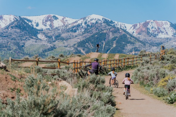 Children and an adult bike on a dirt trail through a scenic landscape with mountains in the background.