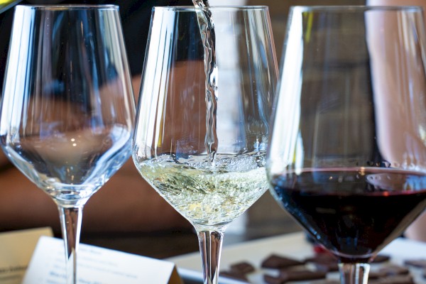Wine glasses, with one being filled, are displayed on a table, alongside a menu and chocolates.