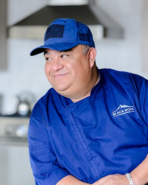 A man in a blue chef's uniform and cap, leaning on a kitchen counter, with a 