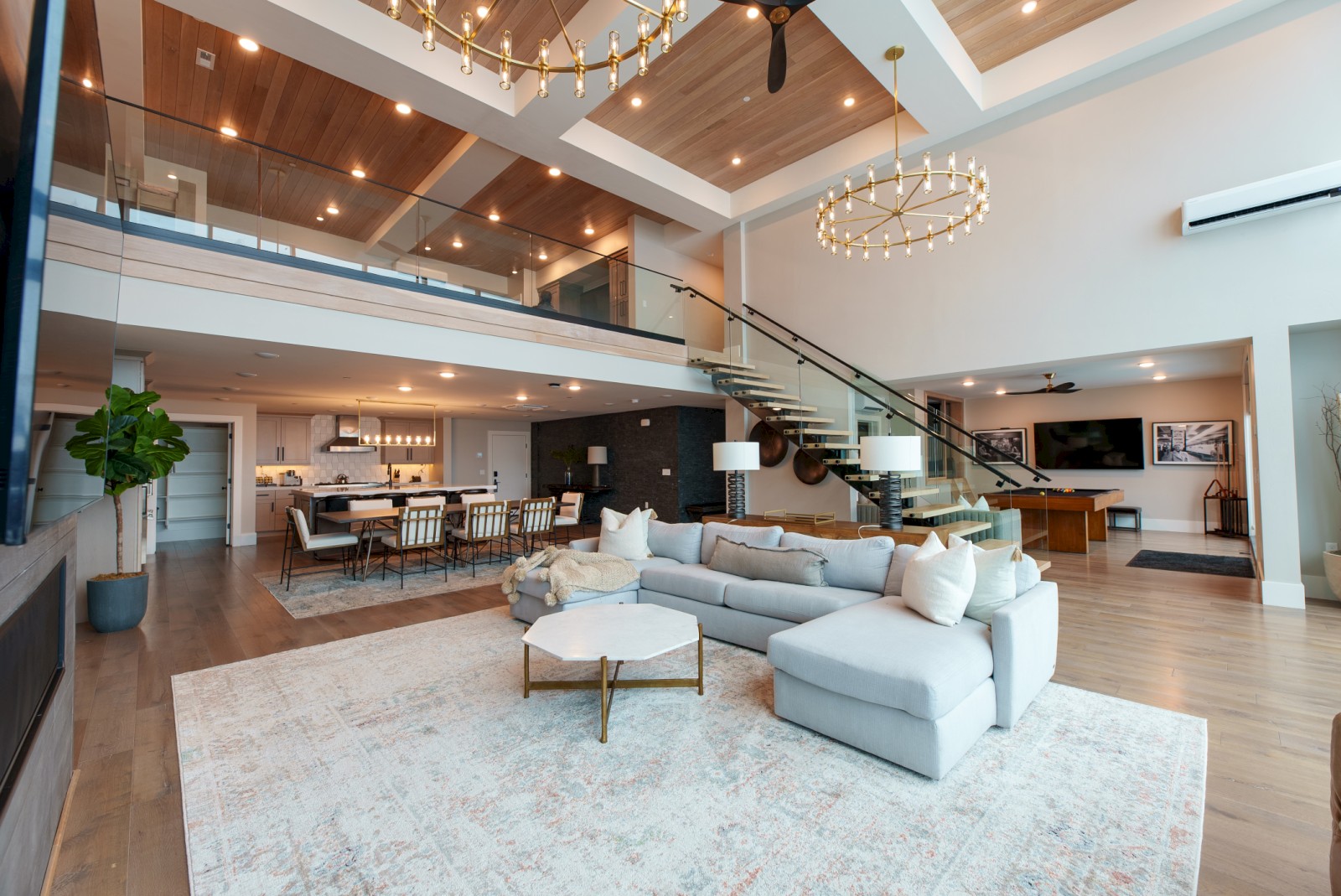 A spacious, modern, two-story open-plan living area with stylish furniture, a kitchen, dining space, and elegant lighting.