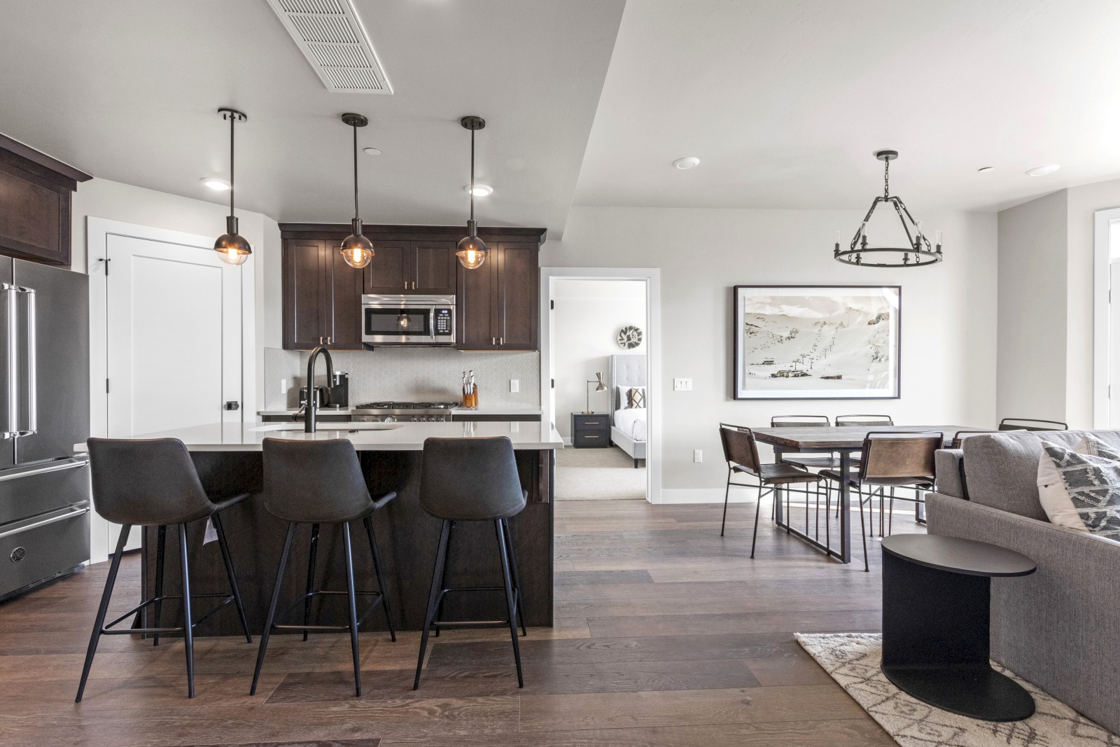 A modern open-concept kitchen and living area featuring dark wood cabinets, black countertops, and contemporary furnishings with natural light.