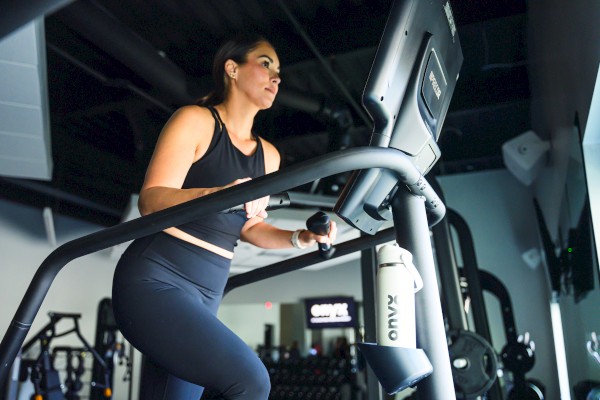 A woman in black workout clothes runs on a treadmill in a gym.