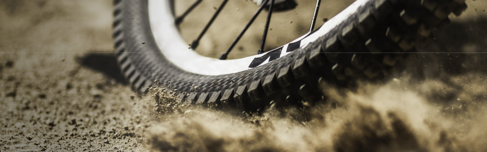A mountain bike tire is kicking up dirt on a rough trail.