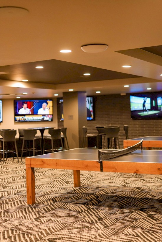 A cozy, modern entertainment room featuring multiple TVs, table tennis, seating, and a bar area for relaxation.