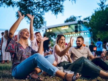 A group of friends enjoying outdoor live music at sunset, sitting on the grass and having fun.