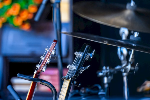 This image shows the headstocks of two electric guitars resting on a stand in what appears to be a music or practice room.