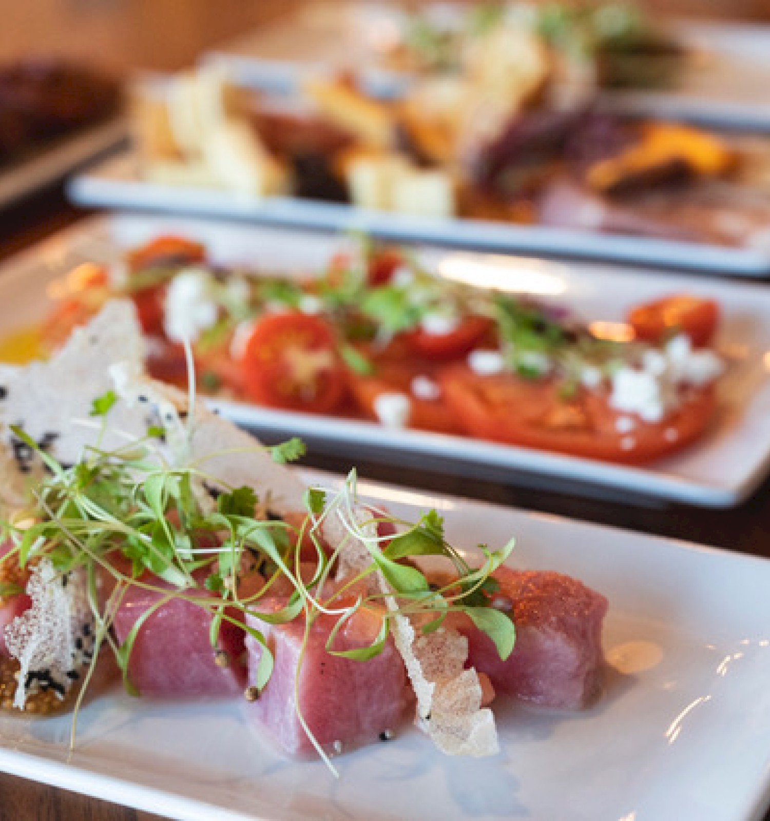 A variety of gourmet dishes, including a plated meat dish with microgreens in the foreground, and other delicious plates in the background.
