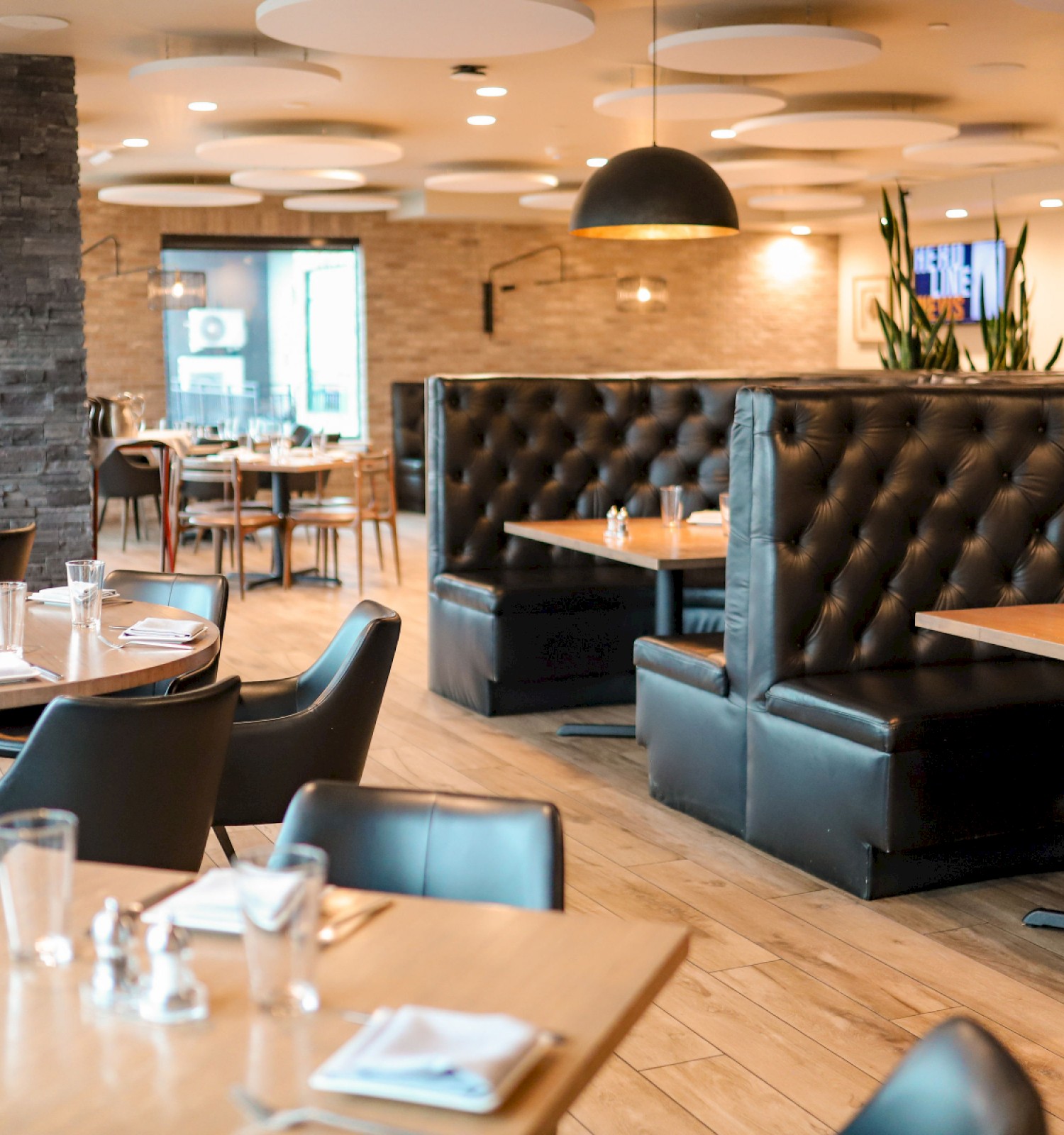 An empty, modern restaurant with wooden tables, black chairs, booth seating, pendant lighting, and a cozy, stylish atmosphere.