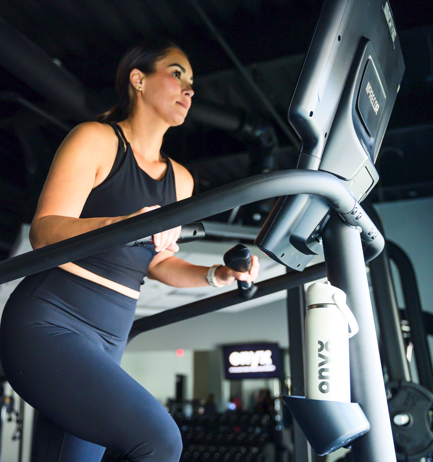 A woman in athletic wear walks on a treadmill in a gym while looking at a screen.