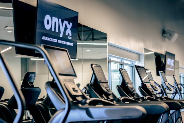 Treadmills are lined up inside a fitness area with screens displaying the Onyx Club at Black Rock Mountain Resort.