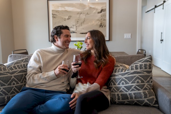 A couple enjoying wine and gazing lovingly at each other on a cozy sofa at home.