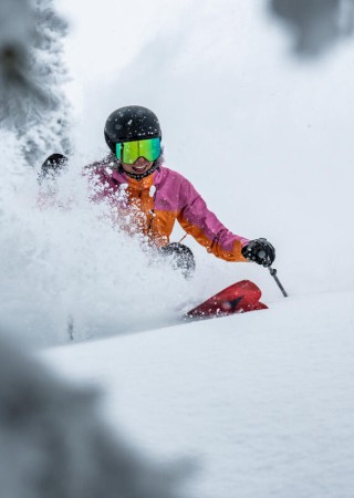 A person in colorful ski gear and a helmet is joyfully skiing through fresh, powdery snow on a winter day.
