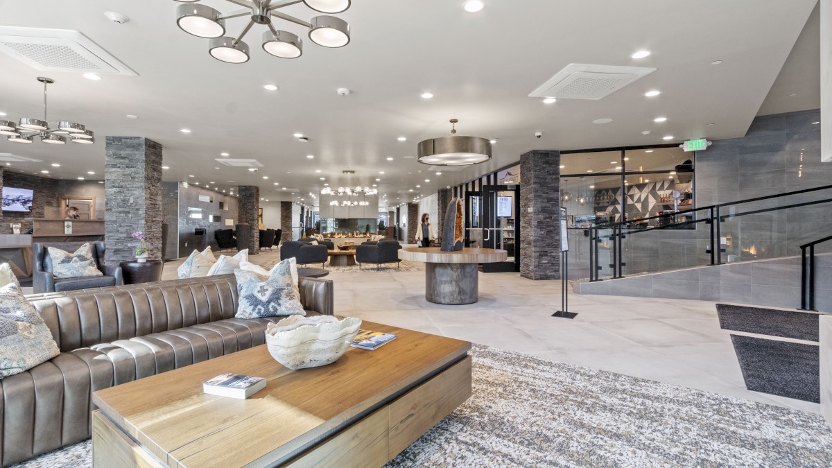 A spacious hotel lobby features modern seating, decorative pillows, a central table with books, and a stylish fireplace in the background.
