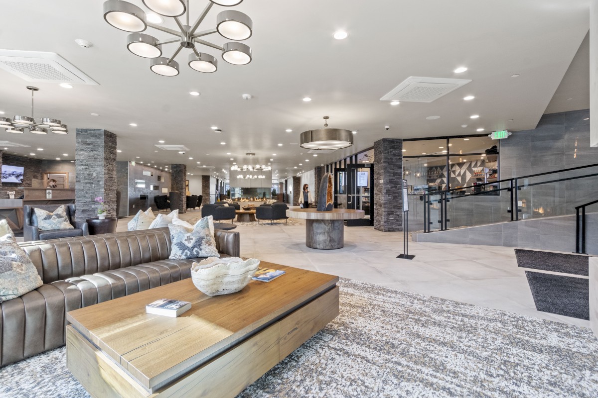 A spacious hotel lobby features modern seating, decorative pillows, a central table with books, and a stylish fireplace in the background.