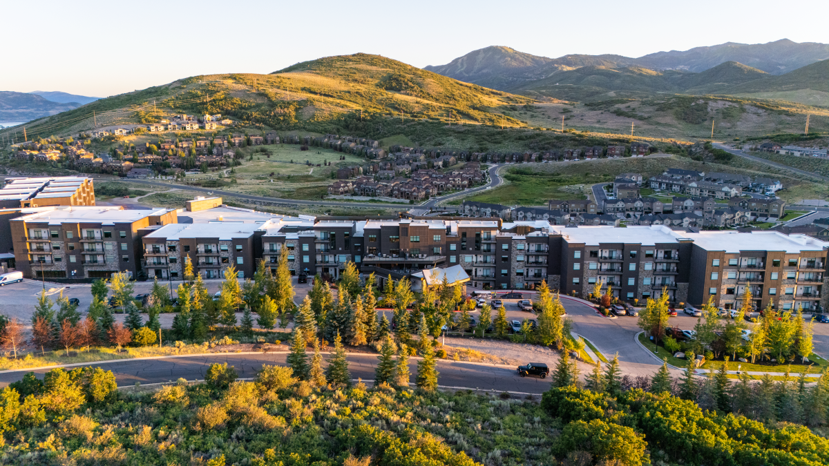 Modern apartment complex with trees, mountains in background, and a clear sky in a scenic, suburban setting.
