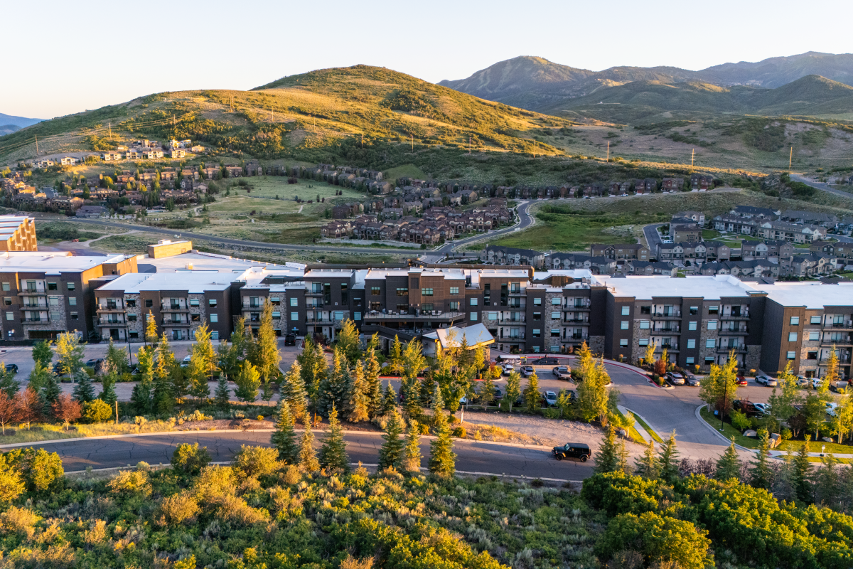 Modern apartment complex with trees, mountains in background, and a clear sky in a scenic, suburban setting.