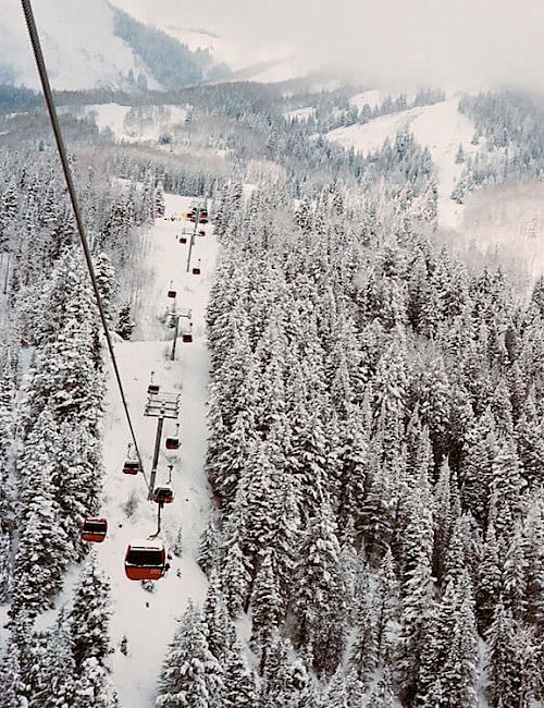 A snowy mountain landscape with a forest covered in snow, featuring a ski lift ascending the slope and carrying people, ending the sentence.