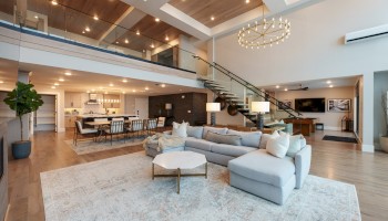 A spacious, modern living room with an open floor plan, featuring a large sectional sofa, high ceilings, and contemporary decor.