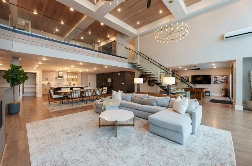 A spacious, modern living room with an open floor plan, featuring a large sectional sofa, high ceilings, and contemporary decor.