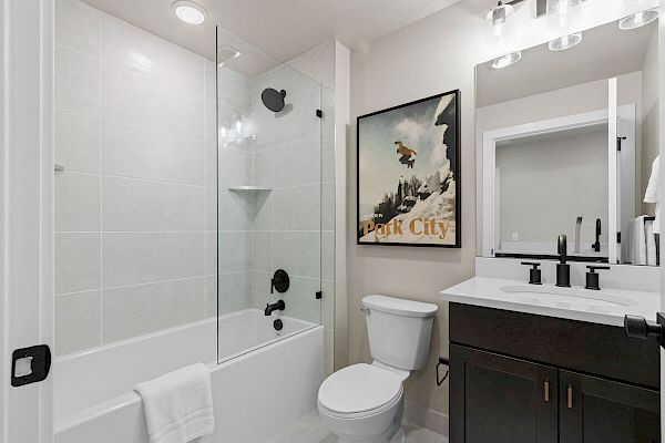 A modern bathroom with a tub-shower combo, toilet, sink with a black vanity, mirrored cabinet, and a wall poster featuring 