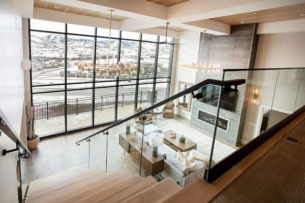 This image shows a modern, spacious living area with a large window offering a scenic view of a mountainous landscape, and a glass railing staircase.