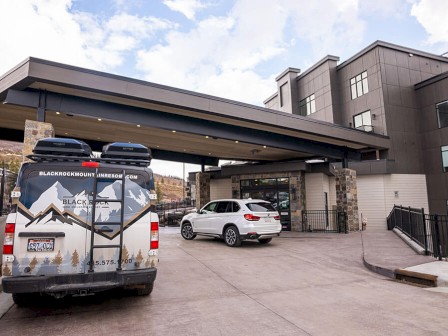 This image shows two parked vehicles, one with graphics, under a modern portico leading to a building. The building has large windows and stone accents.