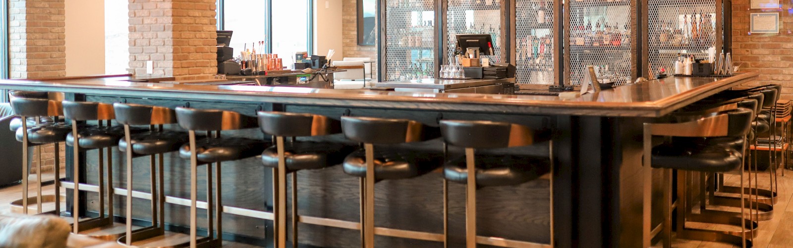 A stylish bar with wooden stools, hanging lights, and a well-stocked back bar return for service. Cozy atmosphere with an inviting setup.