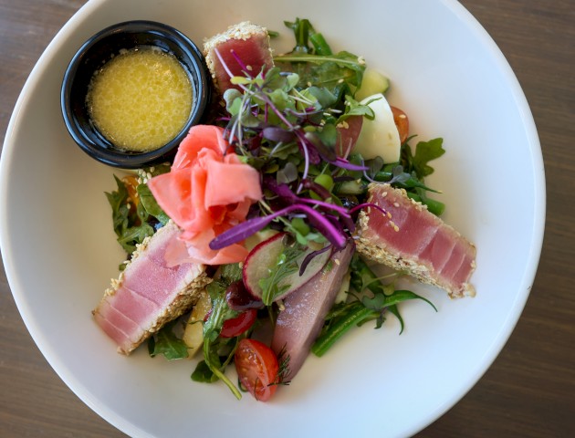 A fresh salad with seared tuna, vegetables, microgreens, and a lemon vinaigrette served on a white plate.