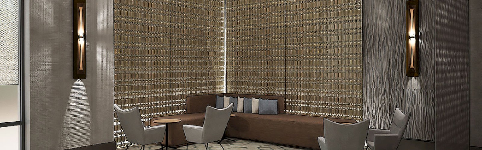 A modern, stylish lobby features a tall, decorated wall, contemporary chandeliers, seating area with chairs and couch, and soft lighting on walls.