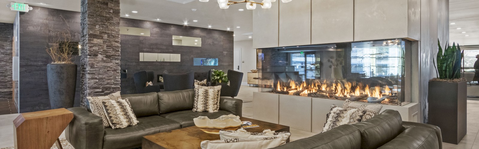 A modern living room with gray sofas, a stylish chandelier, a stone accent wall, a large fireplace, and a mix of wood and white decor finishes the sentence.