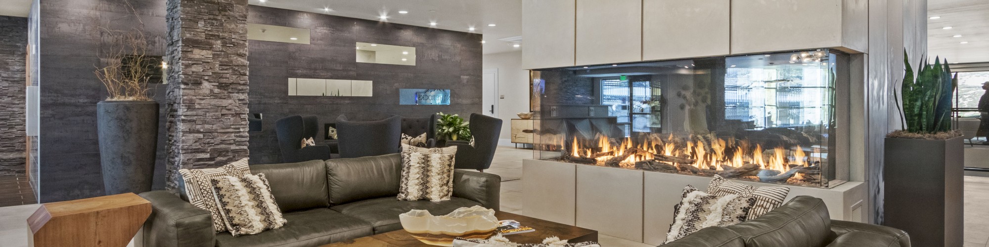 A modern living room with gray sofas, a stylish chandelier, a stone accent wall, a large fireplace, and a mix of wood and white decor finishes the sentence.