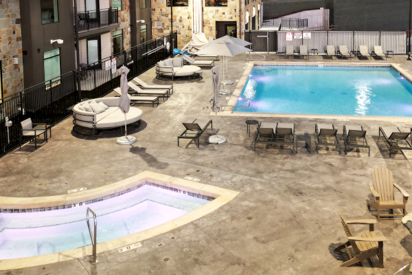 The image shows a pool area with a large rectangular swimming pool and a smaller, circular jacuzzi. There are lounge chairs and daybeds around.