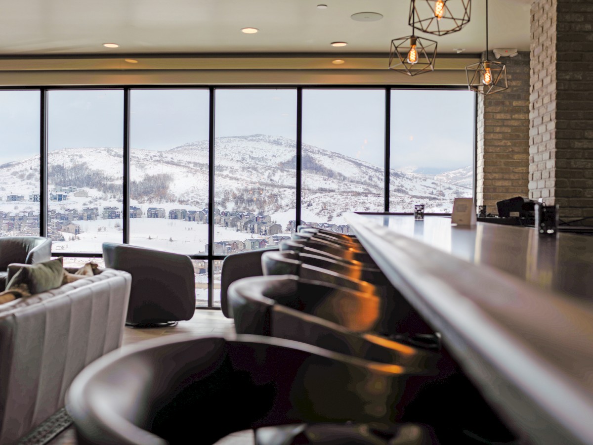 The image shows an elegant lounge with leather chairs and large windows offering a stunning view of snowy mountains, providing a cozy atmosphere.