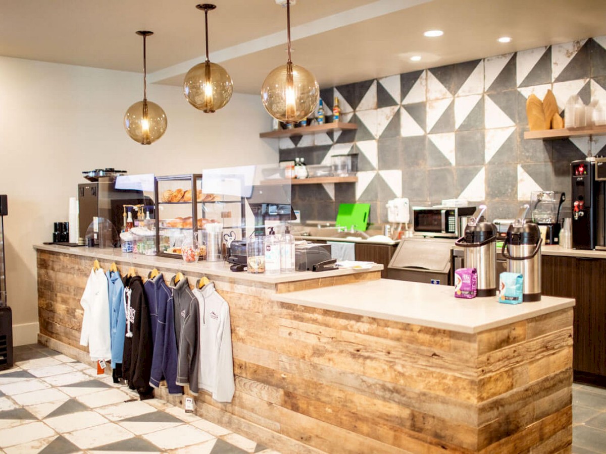 A modern coffee shop with a wooden counter, hanging lights, a geometric-patterned wall, and shelves holding various items. Ends the sentence.