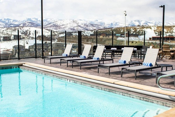 An outdoor pool with lounge chairs on a deck overlooks a snowy landscape and mountains in the background.