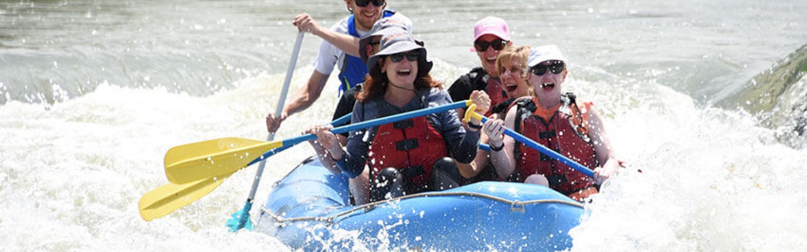 A group of people wearing life vests is whitewater rafting in a river, joyfully paddling through the rapids, surrounded by lush greenery.