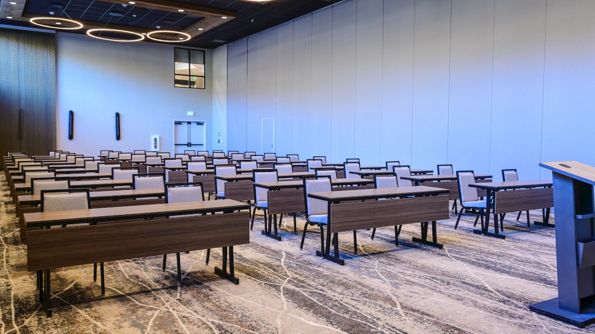 A modern conference room with rows of wooden benches, a podium at the front, blue-tinted wall lights, and circular ceiling lamps overhead.