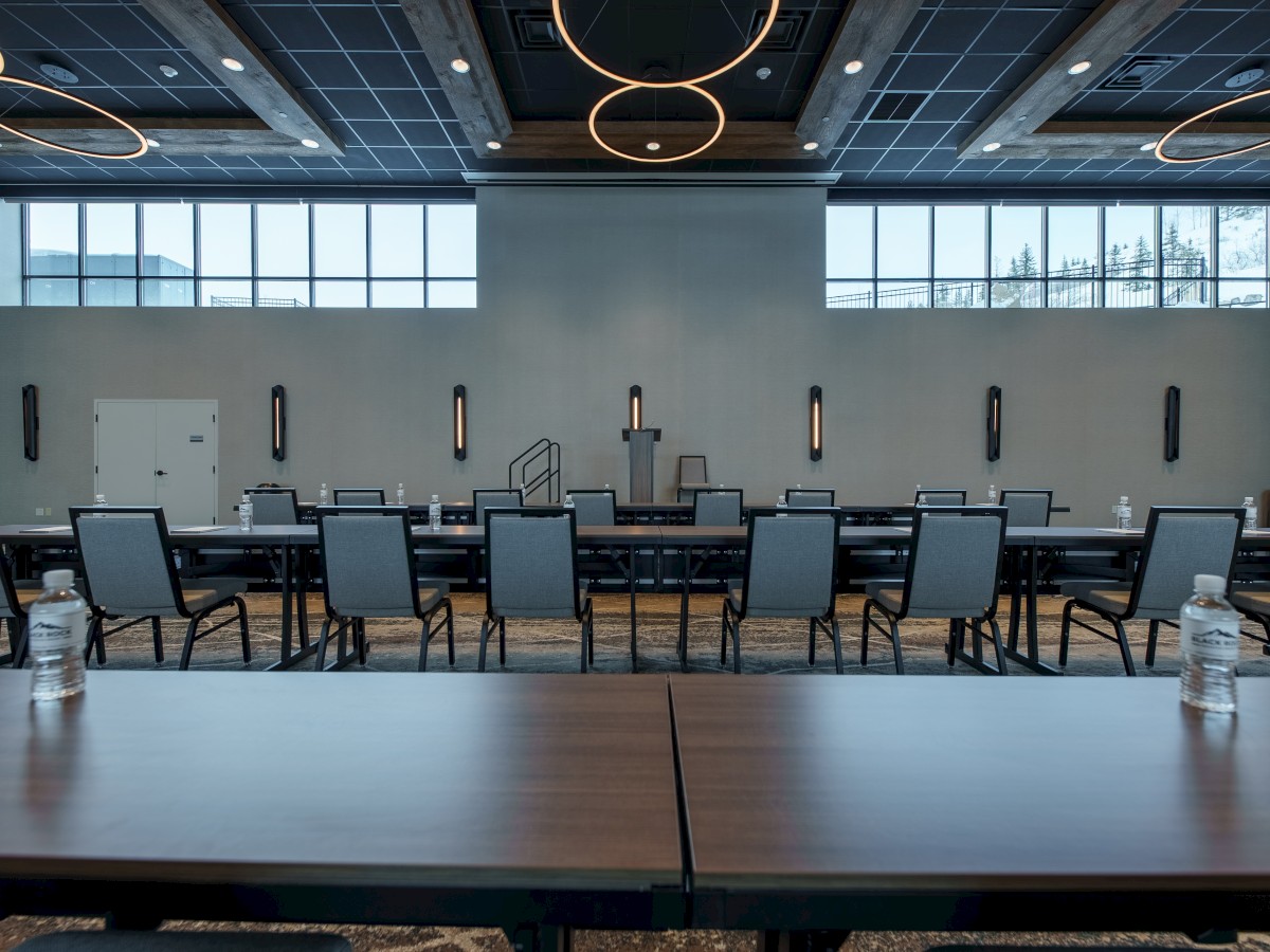 A modern conference room with rows of tables and chairs facing a podium; water bottles and note papers are placed on the tables.