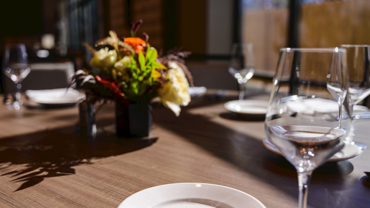 A stylish dining table set with empty plates, wine glasses, and a small flower centerpiece in a softly lit restaurant.