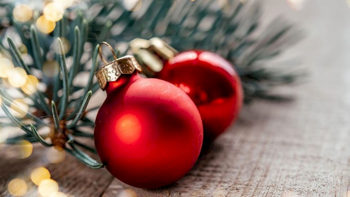 Red Christmas ornaments and pine branches on a wooden surface, with soft golden lights in the background creating a festive atmosphere.