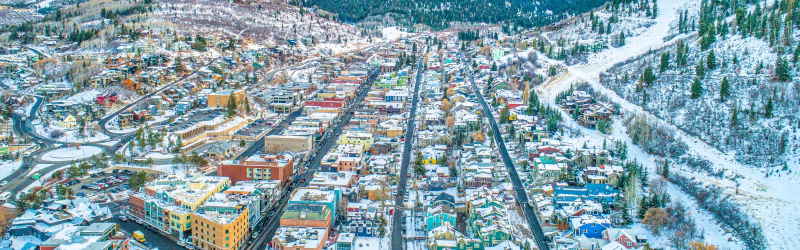 A snowy town nestled between mountains, featuring colorful buildings, a central street, and a backdrop of a stunning, vibrant sky.