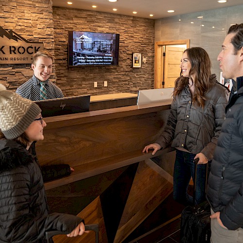 A family is checking into Black Rock Mountain Resort at the reception desk while the receptionist assists them with a smile, wearing winter gear.