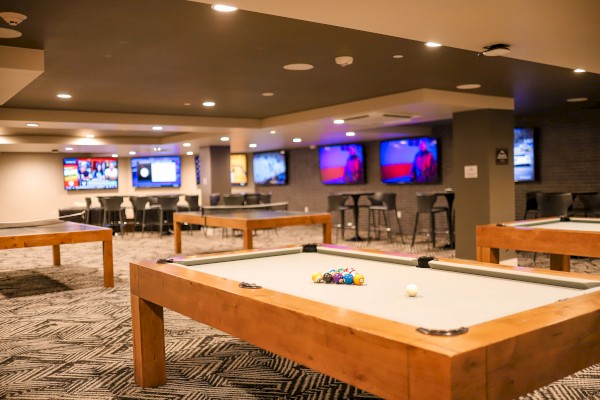 The image shows a game room with pool tables and multiple TVs on the walls showing different broadcasts, creating a casual entertainment space.