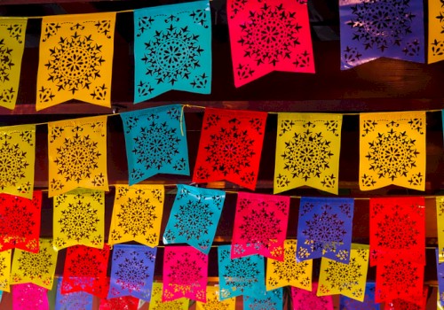 The image shows colorful papel picado decorations with intricate patterns, typically used in Mexican festivities and celebrations.