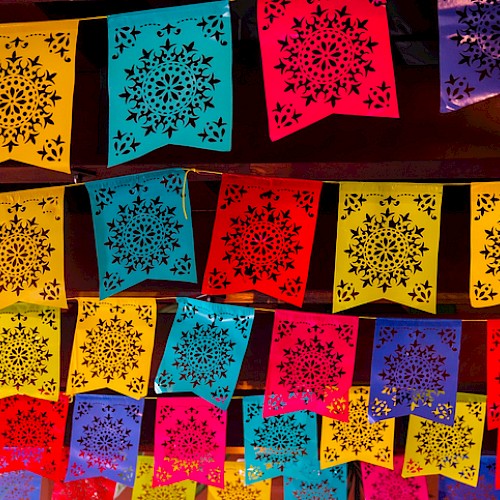 The image shows colorful papel picado decorations with intricate patterns, typically used in Mexican festivities and celebrations.