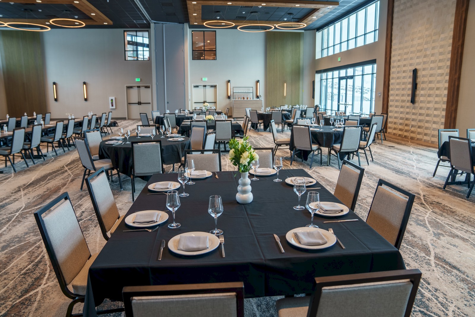 This image shows a banquet hall set up with round and rectangular tables, each adorned with table settings and floral centerpieces, ending the sentence.
